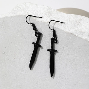 Cool black dagger earrings made of metal hung against a white textured rock background