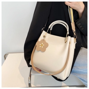 Detailansicht der cremefarbenen Eimertasche mit Goldgriff und Blumenanhänger