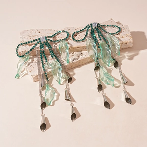 Detail of green rhinestone bow earrings with long tassels and resin leaf accents