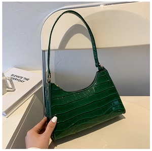 Detail of dark green crocodile texture underarm bag with zipper on minimalist background
