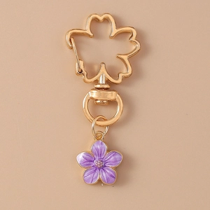 Close-up of golden sakura keyring with purple enamel flower pendant on khaki background