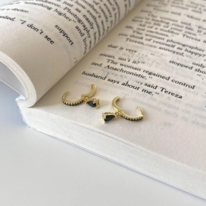 Close-up of gold earrings with black zircon stones resting on a book page