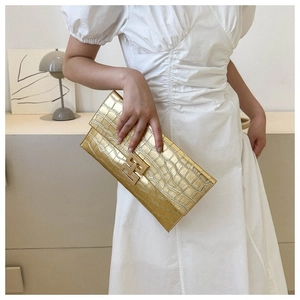 Detail of gold envelope clutch bag with crocodile pattern and geometric metal buckle