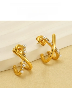 Close-up of golden X-cross pearl earrings with crystals on a textured beige stand