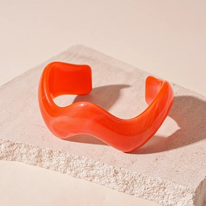 Detail of orange wavy acrylic cuff bracelet with marble texture on beige stone