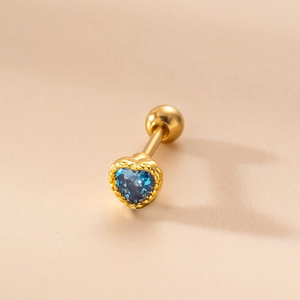 Vista macro de un piercing dorado con circonita azul en forma de corazón y cierre de bola