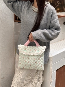 Detailed shot of a green quilted laptop bag with rabbit print and white lace trim detail