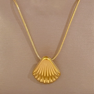 Detailed macro view of gold shell pendant with textured ridges on sleek snake chain