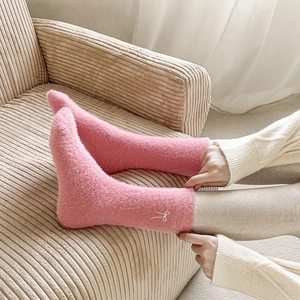 Detail of pink fleece socks with white bow embroidery on a textured velvet fabric