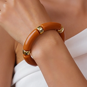 Dettaglio del bracciale in acrilico arancione con distanziatori in metallo dorato lucido sul polso
