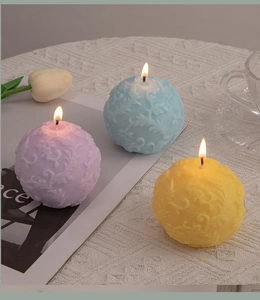 Close-up of three colorful spherical scented candles with detailed floral relief on lace