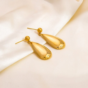Close-up of high-polish gold teardrop earrings on smooth white silk fabric background