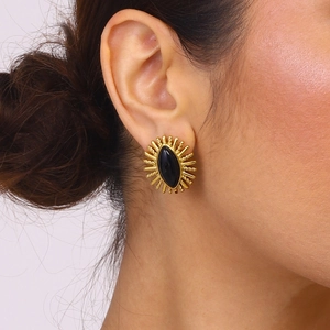 Close-up of vintage black onyx stud earrings with gold sunburst design on a model