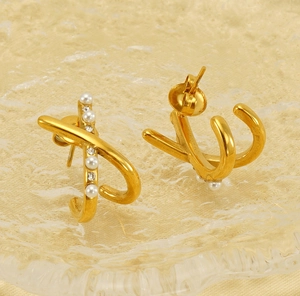 Macro detail of gold letter earrings featuring white pearls and crystals on silk fabric
