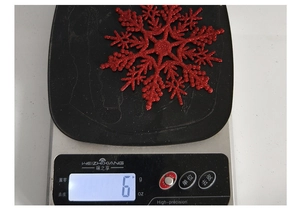 Detail showing a 10cm red glitter plastic snowflake weighing exactly 6g on a digital scale