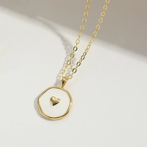 Macro detail of a heart symbol pendant necklace with gold plating and white enamel finish