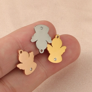 Three tiny angel-shaped mirror steel pendants with diamonds shown on a finger