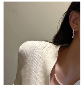 Close-up of minimalist silver water drop earrings and elegant white pearl necklace on model