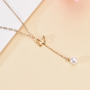 Minimalist gold butterfly pendant necklace with a pearl drop on a neutral background