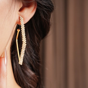Vista laterale di eleganti orecchini curvi in oro con micro-diamanti su una modella