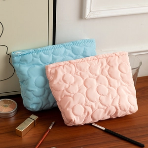 Dettaglio della texture floreale trapuntata su borse per cosmetici blu e rosa
