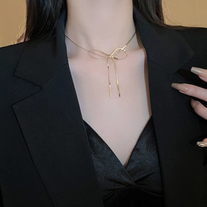 Detail shot of a minimalist golden bow snake chain necklace on a female model