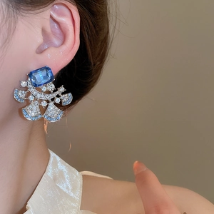 Detailed view of silver needle flower earrings with blue stones and fan-shaped diamonds