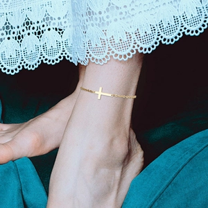 Detailed view of a gold cross anklet worn with white lace skirt on a blue background