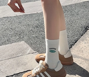 Close-up of white ribbed mid-calf socks with green HAMPIONS embroidery and brown sneakers