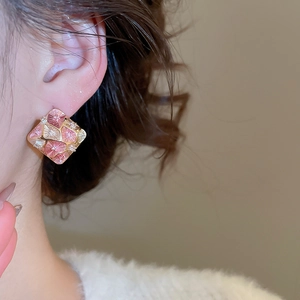 Close-up of elegant gold plated rhombus earrings with pink enamel flowers on a model