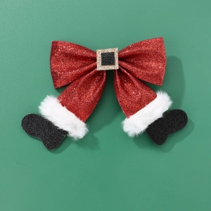Detail view of a glittery red Christmas bow hair clip with Santa boots on dark green background