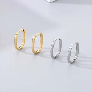 Polished geometric oval hoop earrings in gold and silver finishes on a grey background