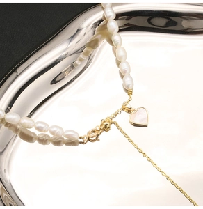 Macro shot of natural baroque pearls with a heart-shaped gold pendant on mirror