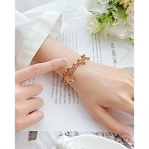 Detail of a layered rose gold stainless steel bracelet with a heart pendant on a woman wrist