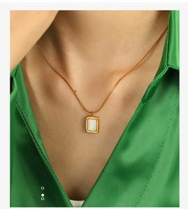 Détail du collier pendentif en nacre dorée porté sur un col de chemise en soie verte