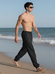 Detail of men's drawstring linen joggers showing tapered cuffs and draped fabric on beach