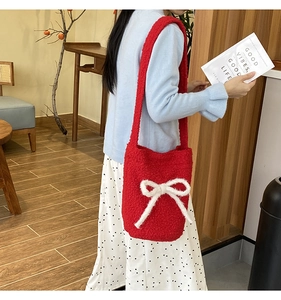 Red plush bucket bag with white bow detail shown in a cozy lifestyle setting