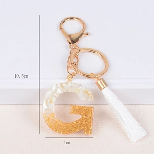 Detail view of resin letter G keychain with gold foil, white tassels and 10.5cm scale