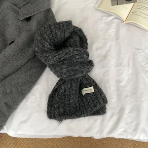 Close-up of thick dark grey wool knit scarf with brand label on a cozy winter bed