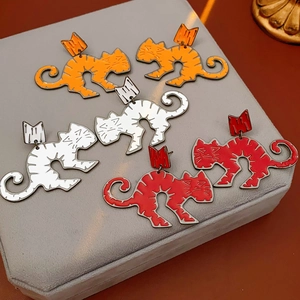 Detailed close-up of cartoon cat earrings in orange, white and red on velvet pad