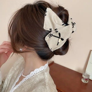 Detail of beige fabric bow hair claw with black embroidery and gold tag in hair