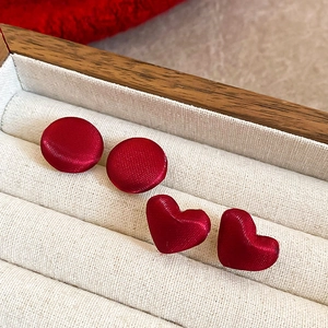 Dettaglio di orecchini a lobo tondi e a cuore in tessuto rosso in un portagioie di legno