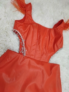 Détail d'une robe en similicuir orange avec bordure en plumes et franges de strass brillants