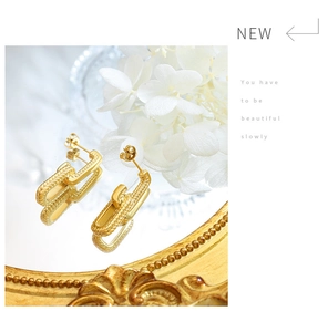 Detail view of gold-plated geometric U-shape earrings on a vintage mirror surface