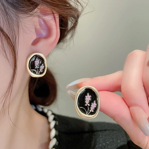 Macro detail of irregular gold-plated earrings with black enamel and purple floral accents