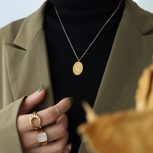 Gold oval flower pendant necklace on model with black knit and green blazer