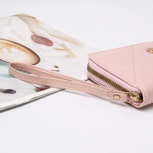 Detail of pink quilted leather long wallet with gold zipper and wrist strap on a white table
