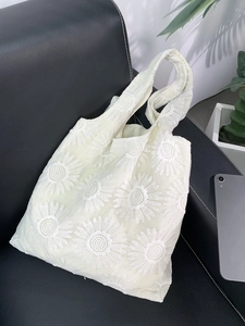 Close-up of intricate daisy flower embroidery on a cream canvas tote bag with 3D texture