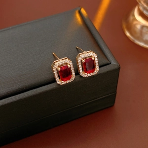 Macro view of gold stud earrings with rectangle red rubies and diamond halos on a black box