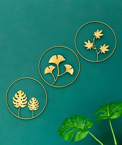 Detail of three-piece golden metal wall art featuring ginkgo and monstera leaf designs